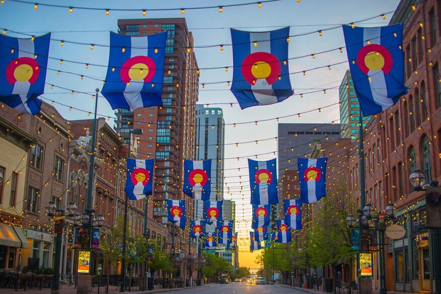 Brightly colored flags strung across the street with multi story buildings in the background.
