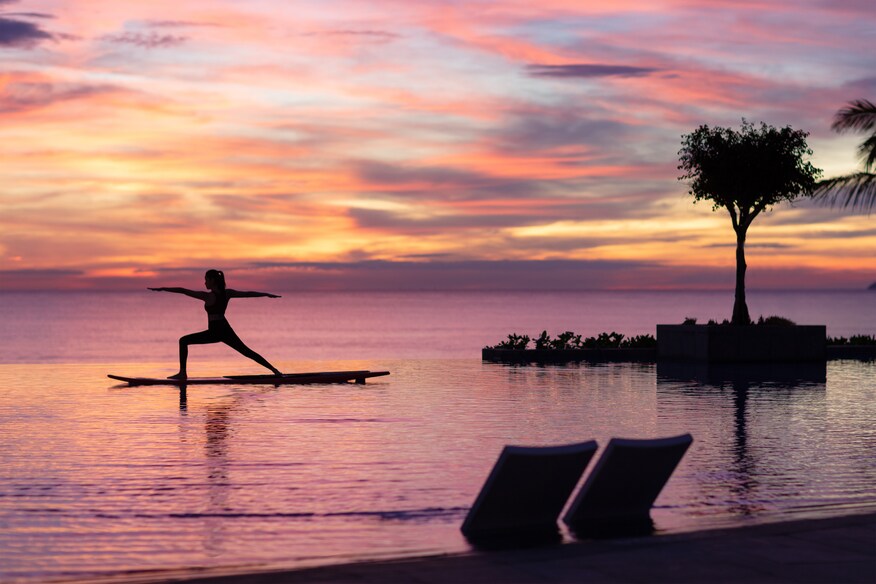 Woman doing yoga on a paddleboard on the ocean at sunrise with a pink and yellow sky