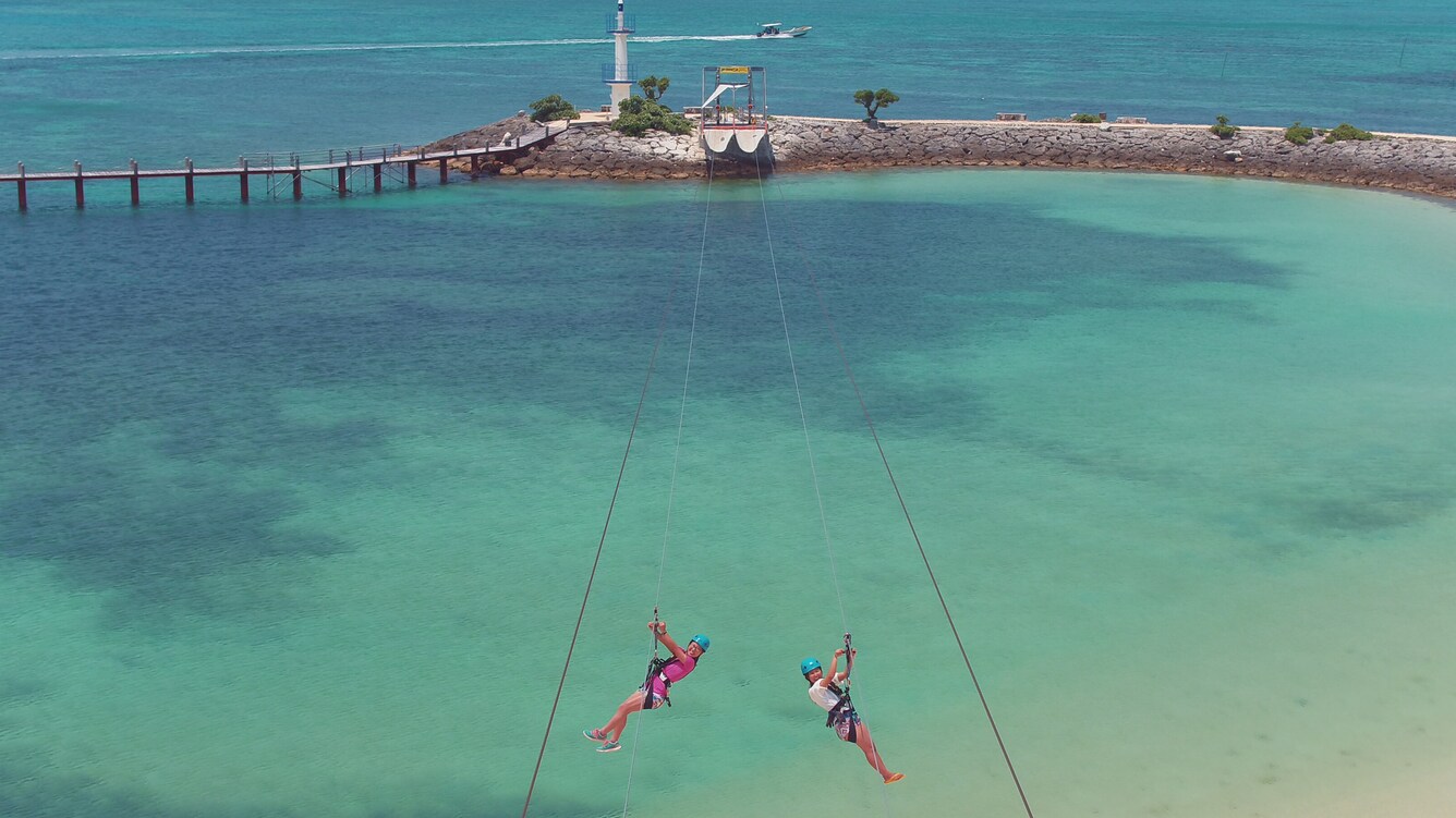 Two people riding a zip line over the water.