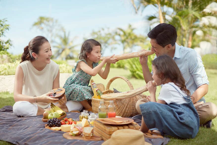 Family having a basket picnic in an idyllic setting with palm trees in background.