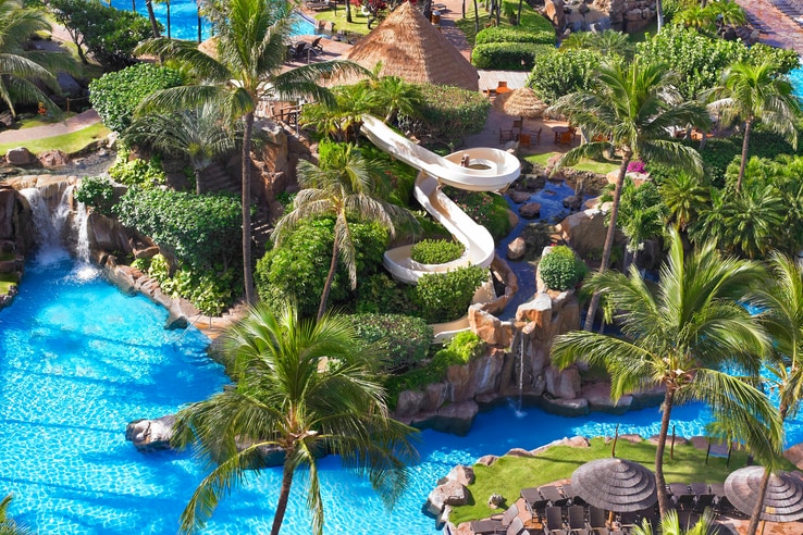 Family pool view from above with waterslide and lush vegetation.
