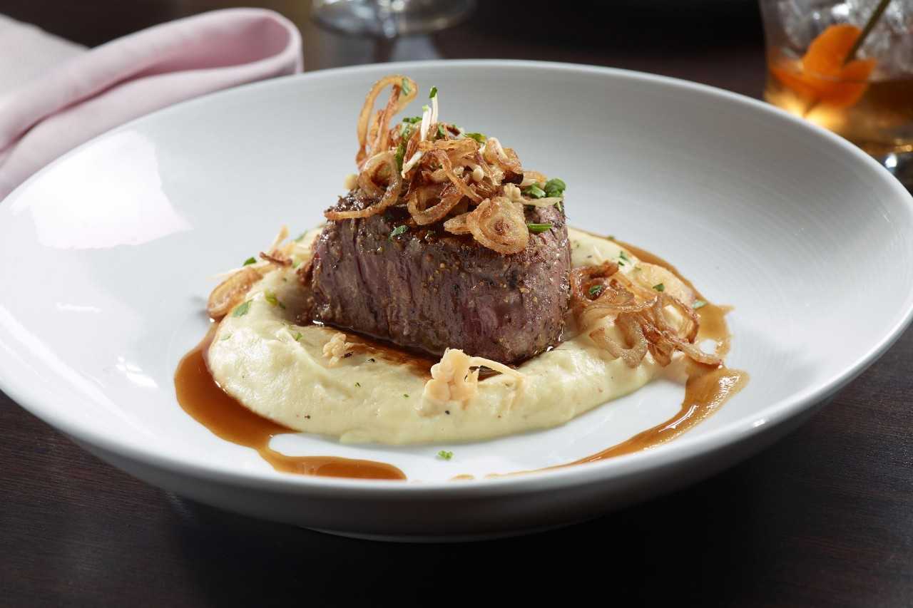 Chunk of beef on mashed potatoes with onion topping.