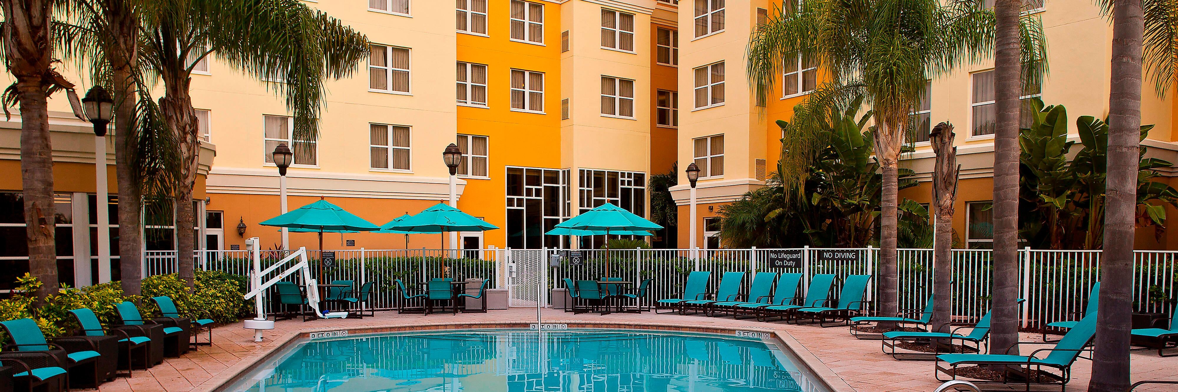 Hotel pool with fenced pool deck, sunchairs, and umbrellas.