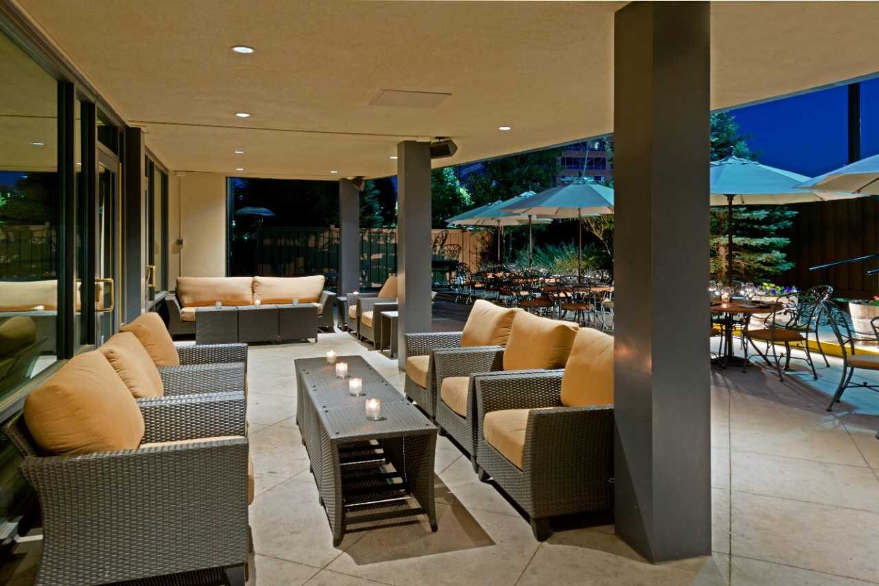 Outdoor patio with padded armchairs, tables with umbrellas, and candle lighting.