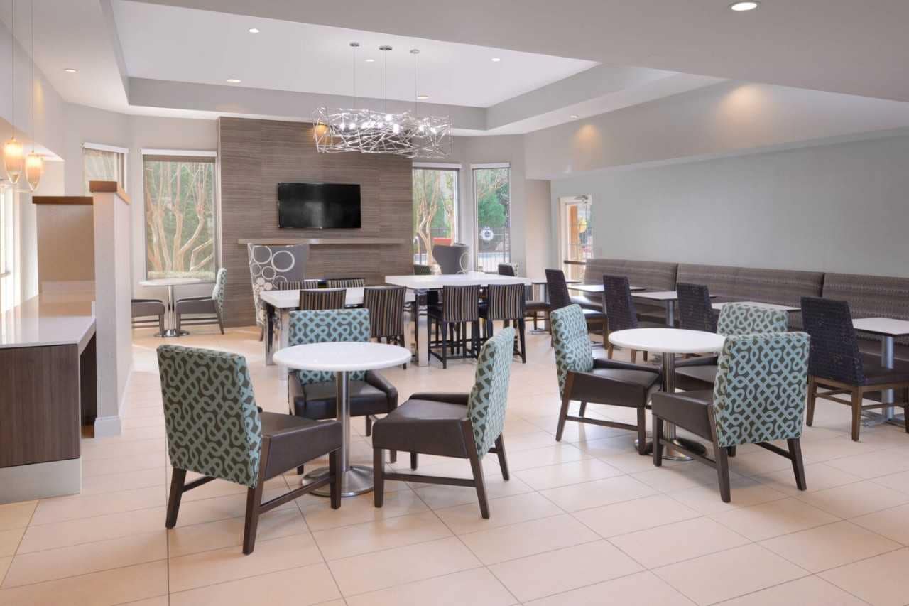 Hotel lobby seating with tables and padded chairs and large windows.