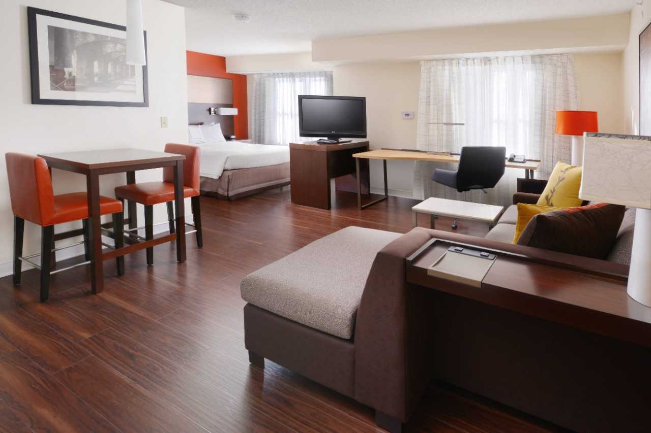 Hotel suite with sofa seating, desk, table with two chairs, bed, and flatscreen television.