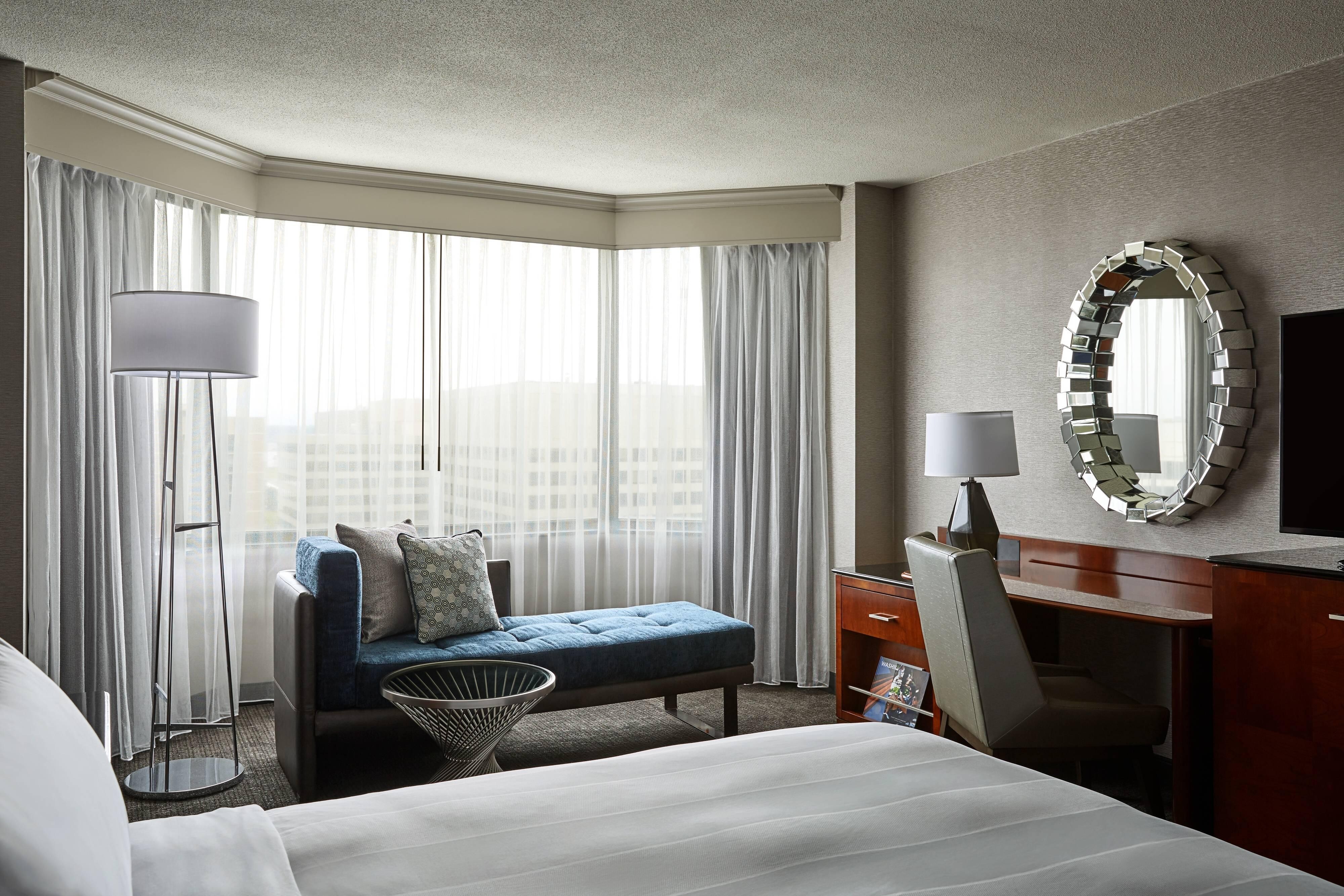 Guestroom with bed, desk, mirror, chaise lounge and bay window
