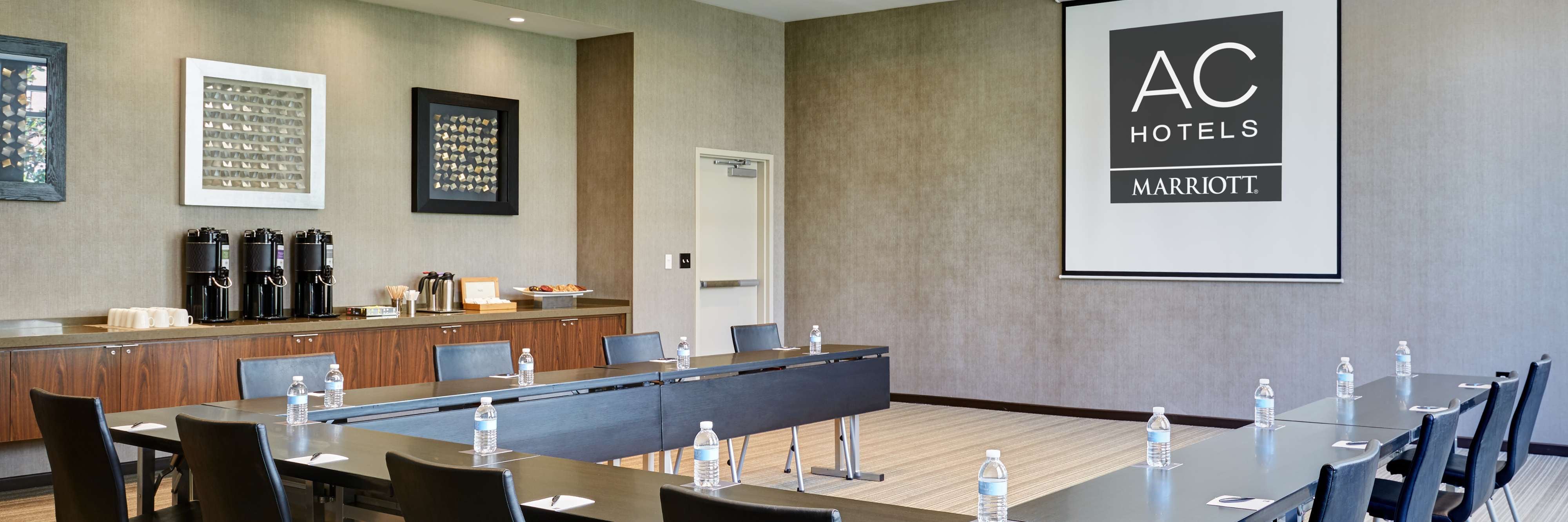 Meeting table set up in a U-shape around a projector screen, with water bottles and a coffee station.