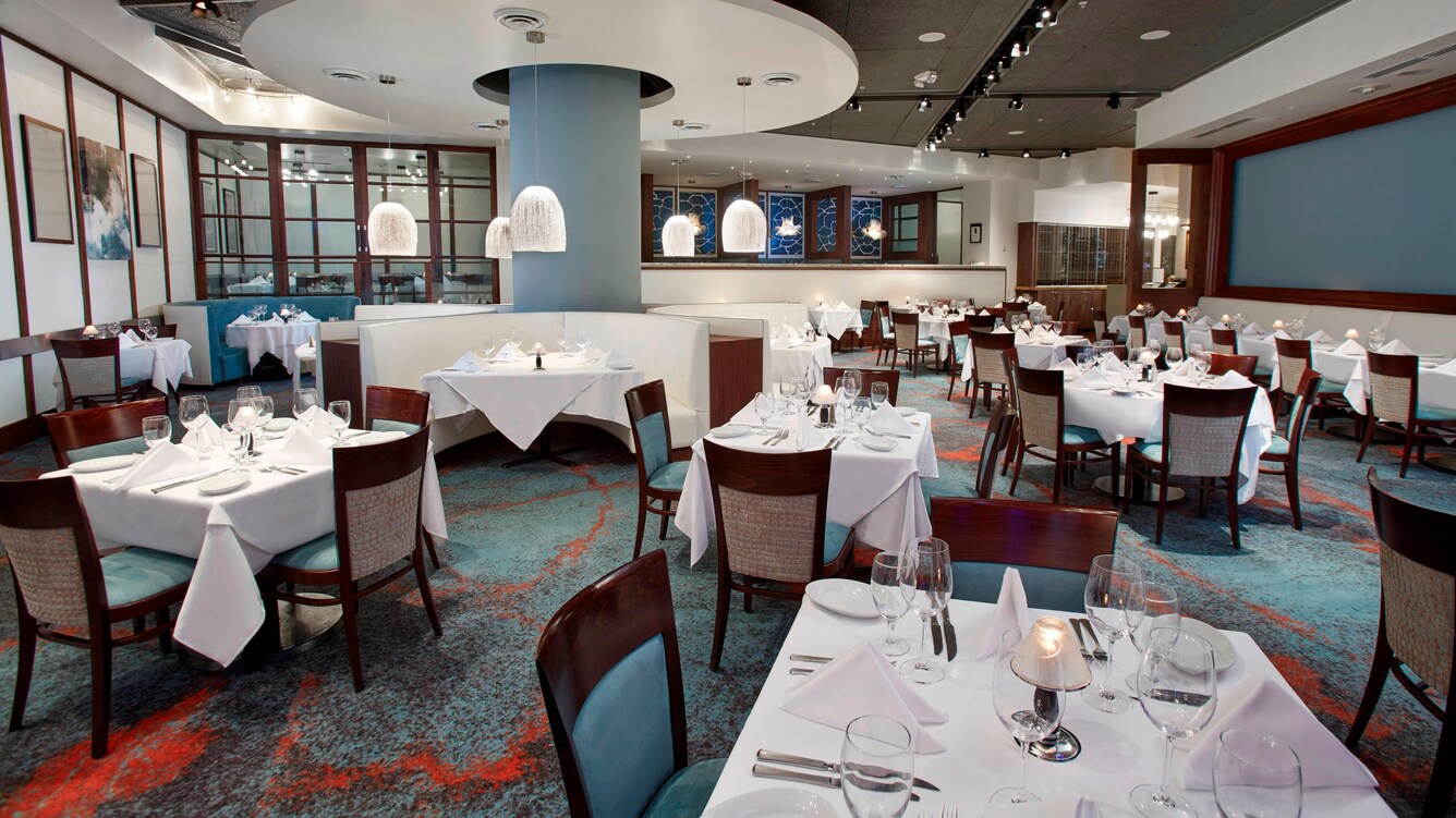 Dining room with blue carpet and tables with white linens.