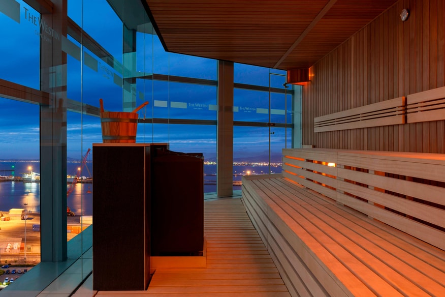 Sauna with wooden bench and windows with view of the city.