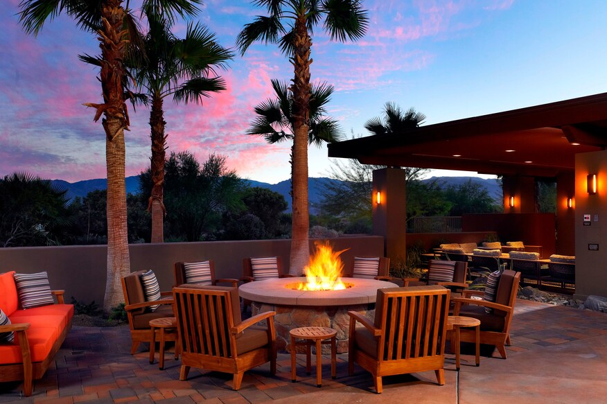 A well-lit fire in the Fire Pit areas, low patio seating, and view of the setting sun.