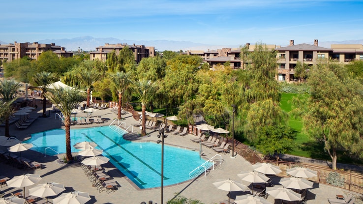 Aerial view of pool area with treeline and resort.