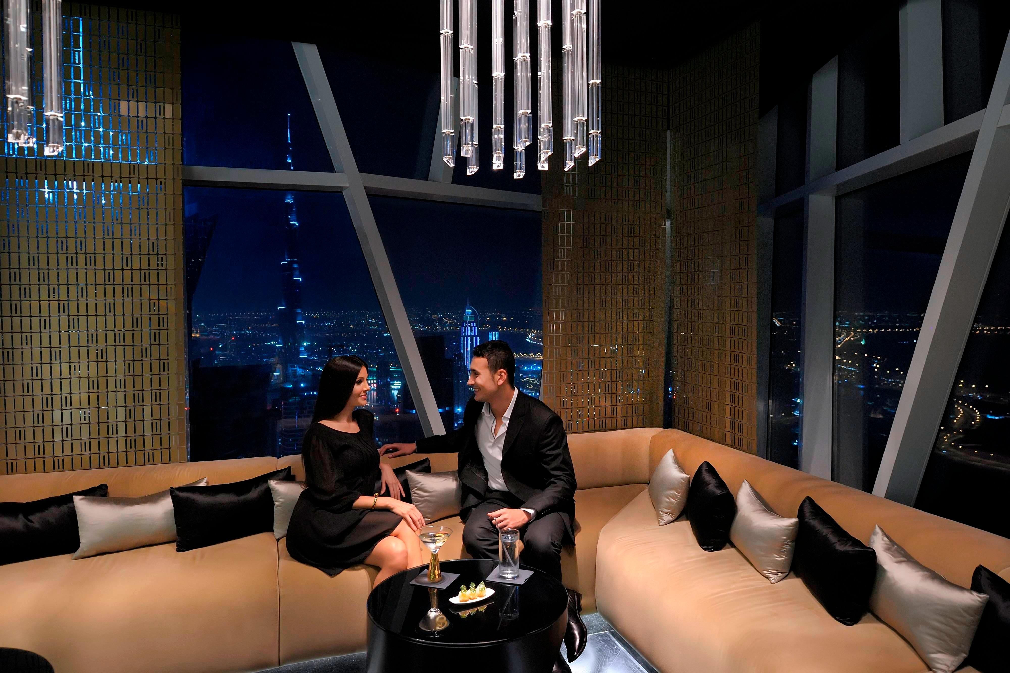 People sitting on sofas near windows with high floor city views at night