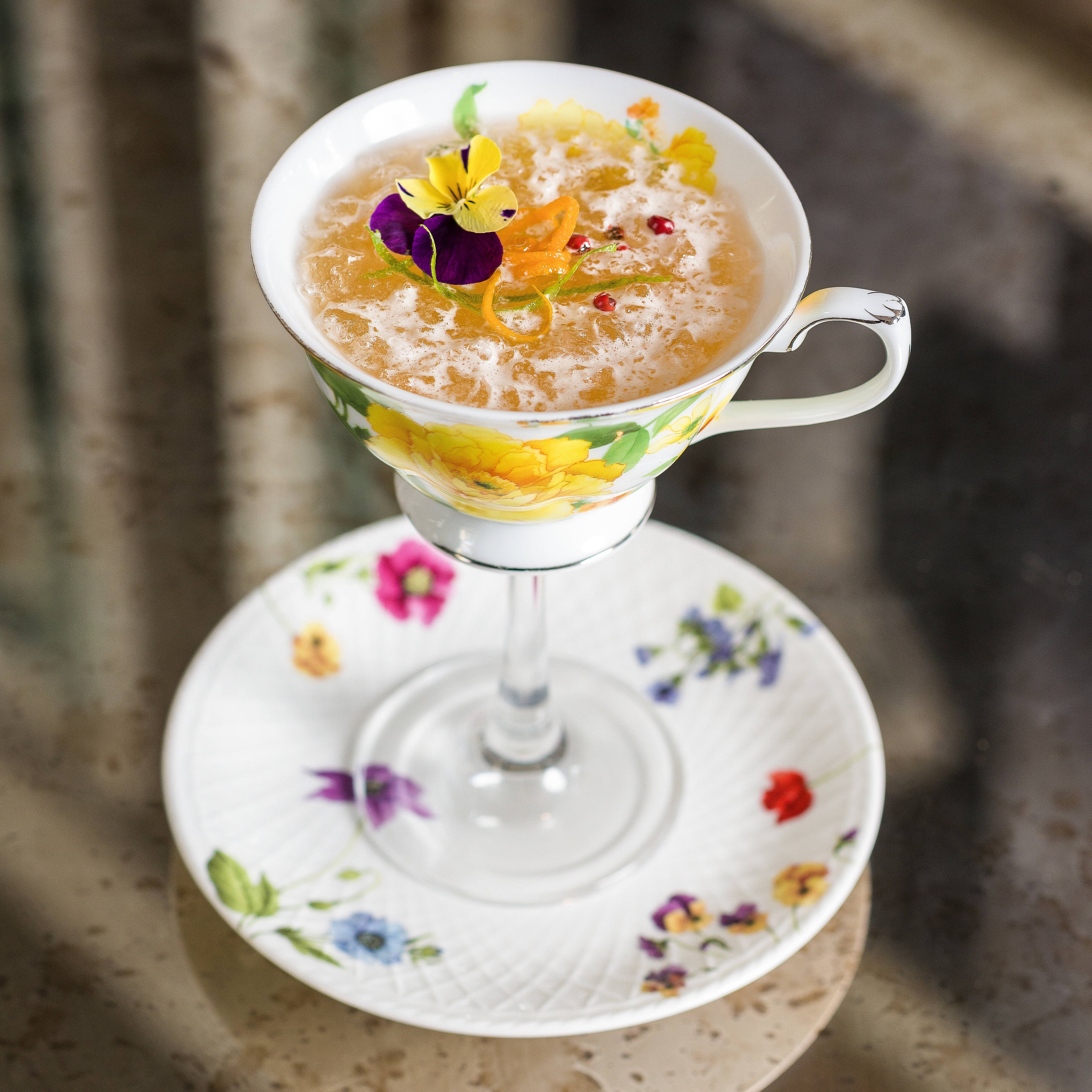 A cocktail garnished with flowers served on a small floral plate