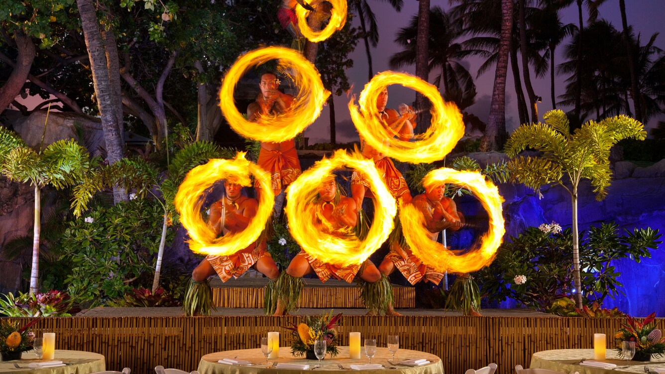 Six men in a pyramid formation swinging flaming knives around in a circle.