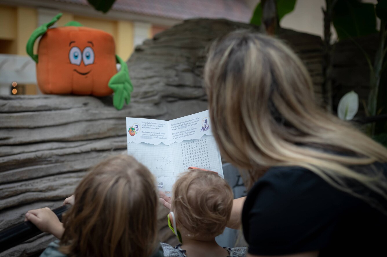 Woman and children looking at scavenger hunt booklet and square pumpkin toy.