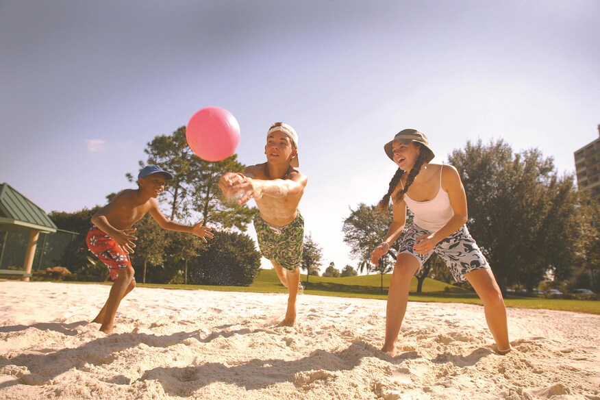 Three girls diving for volleyball in sand.