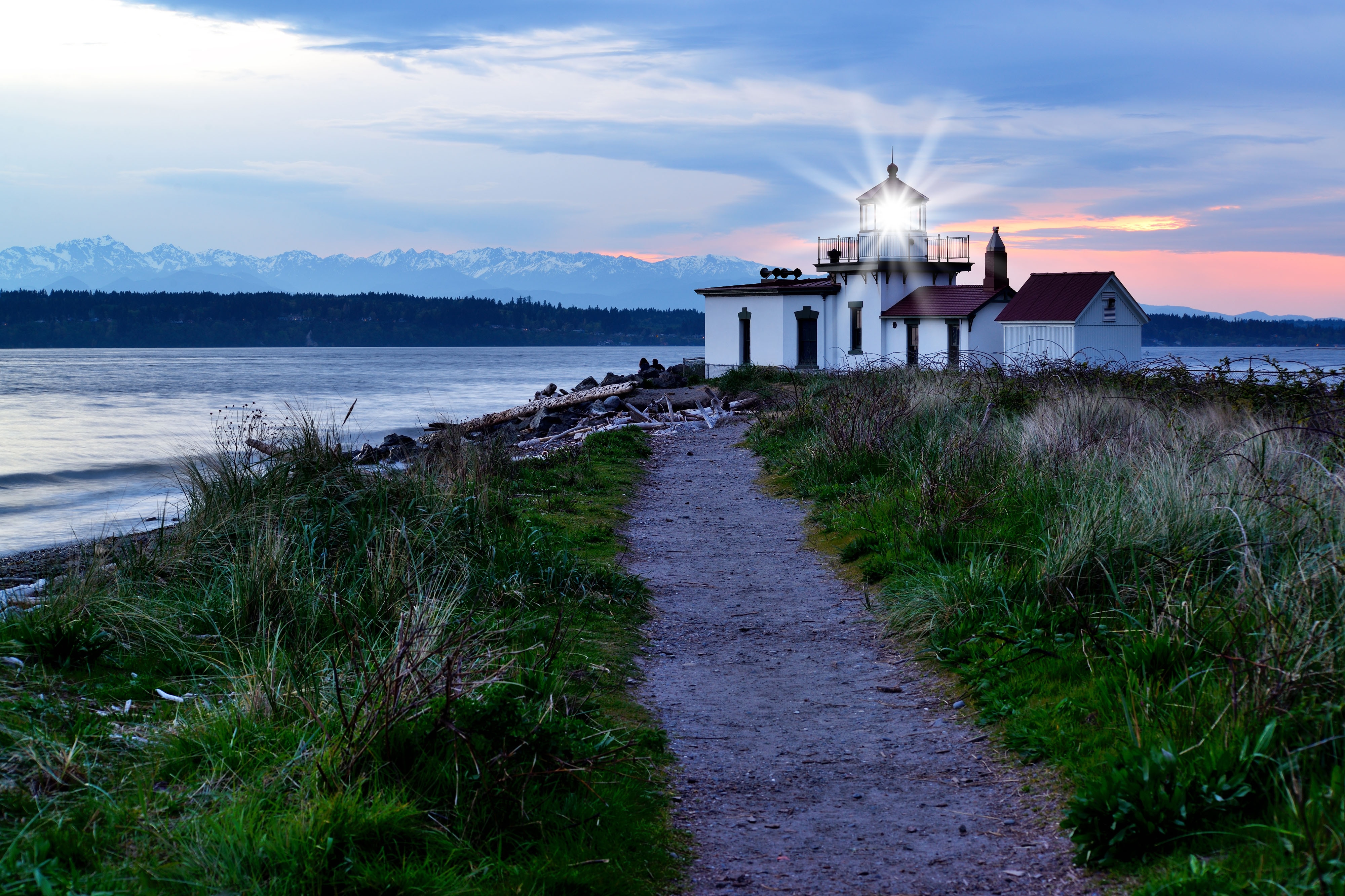 Discovery Park Lighthouse with light burst, at sunset with Olympic Mountains in distance.