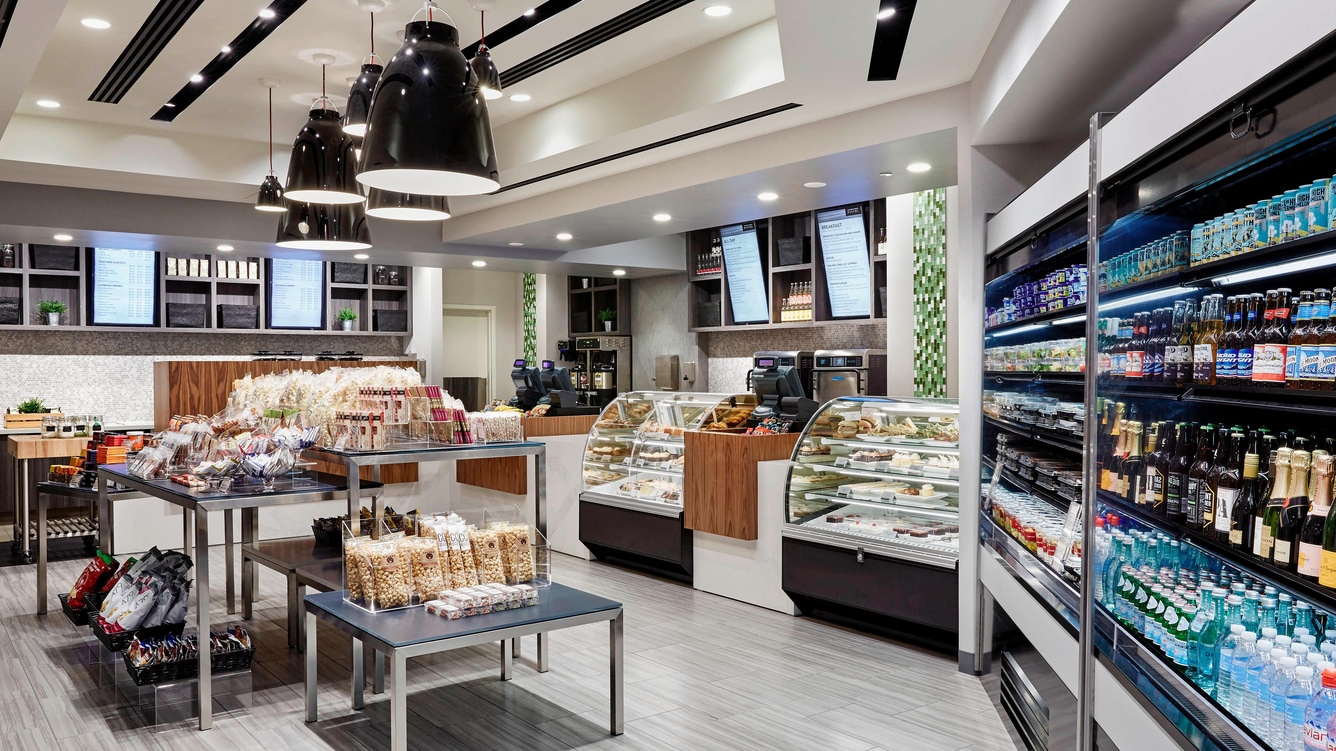Interior of a convenience store with refrigerated drinks and pastries in a glass case.
