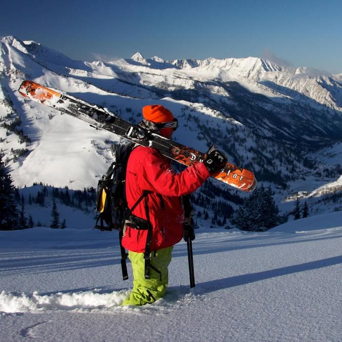 Person carrying their skies on their shoulder in the snowy mountains