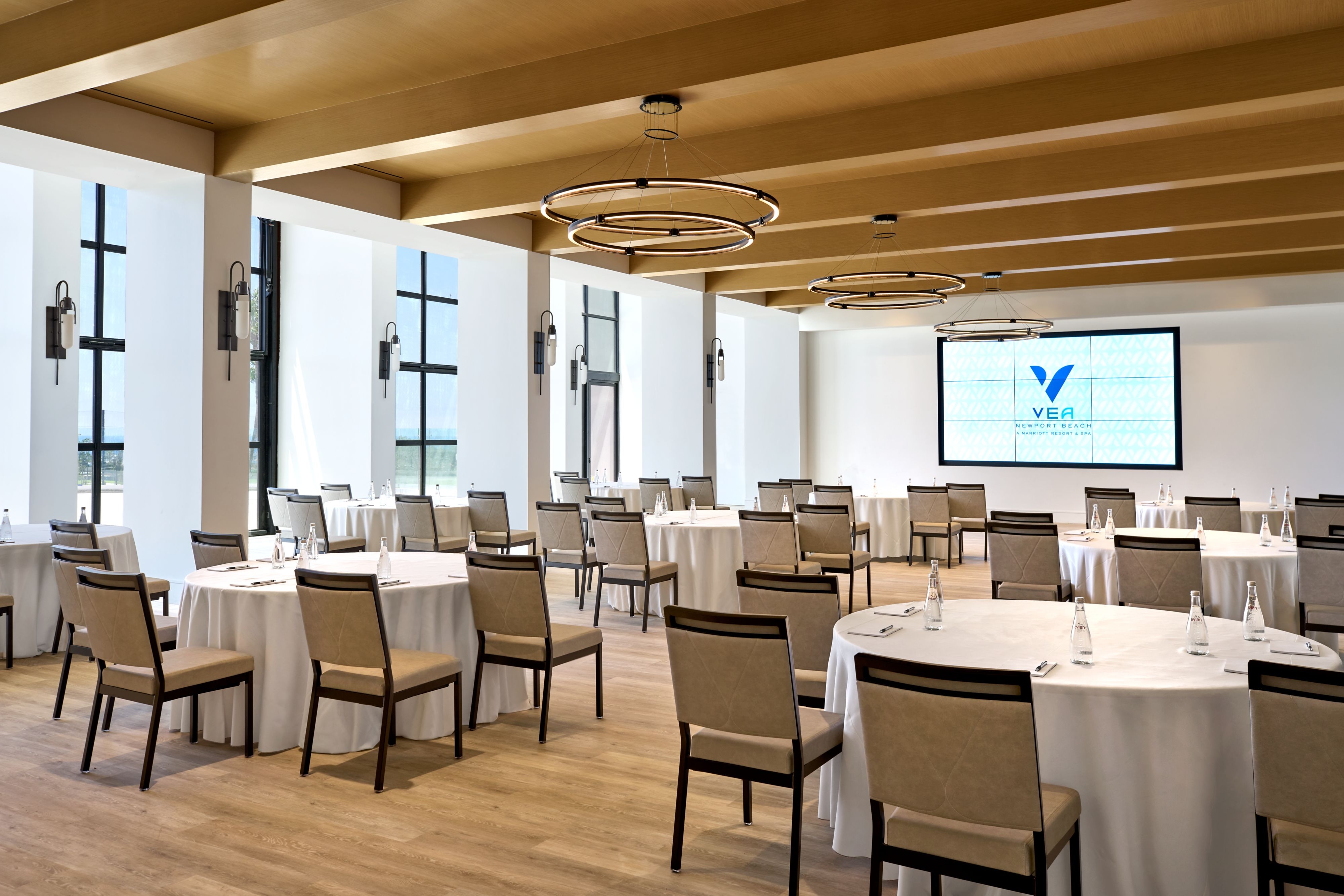 Meeting room with round tables, large windows with exterior views, and a projector screen